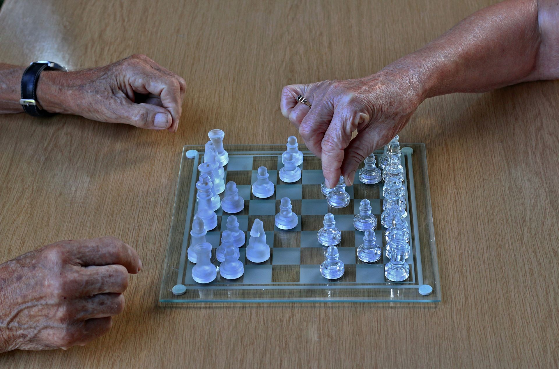 Old wrinkled male hands playing chess with elderly female hands. Concept of active elderly people during retirement. Everyday joy lifestyle without age limitation.