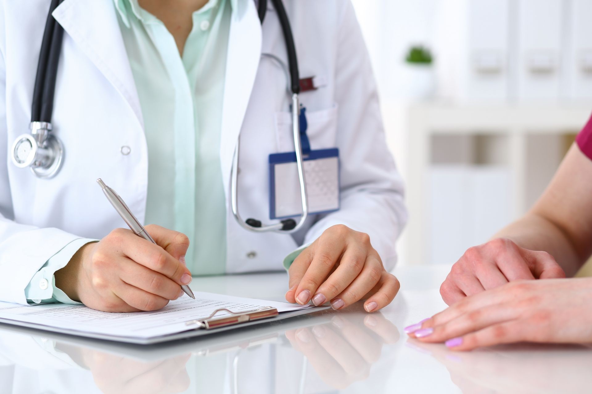 Doctor woman consulting patient while filling up an application form at the desk in hospital. Just hands close-up. Medicine and health care concept